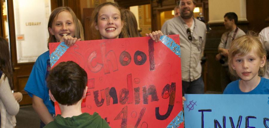 An elementary student smiles and poses with her sign